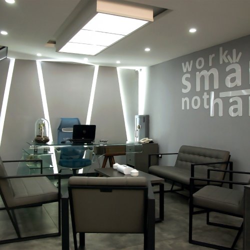 A conference room in an office featuring several chairs and a glass desk. The wall is decorated with a decal.