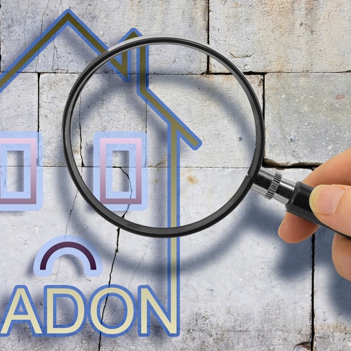 A person holding a magnifying glass up to a drawing of a house with a frowning face and "RADON" printed underneath it.