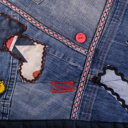 A close-up of a denim jacket covered in colorful applique hearts, chunky thread, and other fabric patterns.