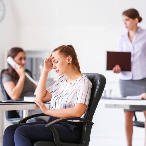 A person looks uncomfortable while sitting in a chair while three more employees continue working behind them.