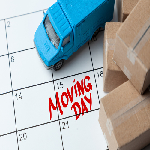 A calendar with a blue toy moving truck and small cardboard boxes on it. Red text on the 15th says "Moving Day."