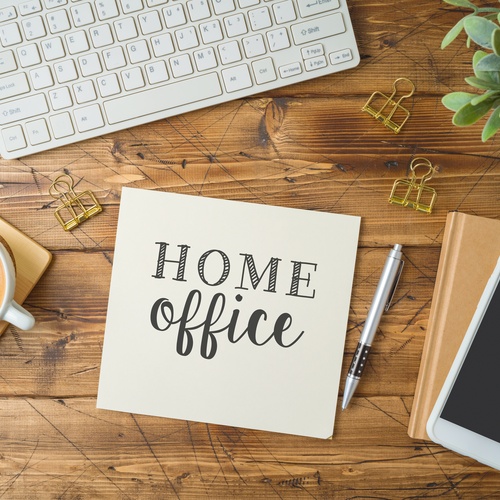 A silver pen rests next to a notepad that says, “Home Office,” beside a white keyboard, coffee cup, and gold binder clips.