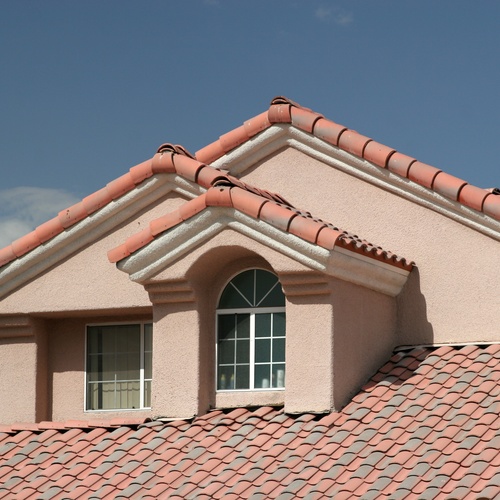 A close-up of a home's roof with three gables and discolored red tiles. The sky above is clear and blue.