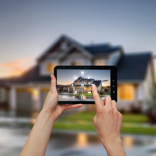 A woman stands outside her home and uses a tablet to control smart home lighting and security systems.