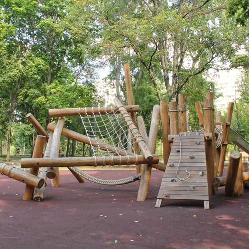 An outdoor playground structure made entirely of wood, with green treetops in the background.