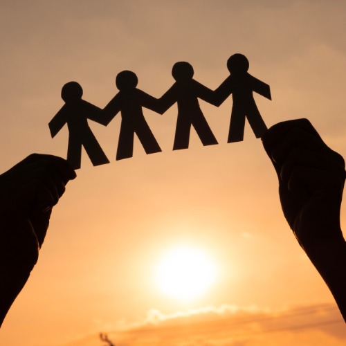 A low-angle view of a silhouetted figure holding a cutout of four connected people against a warm, cloudy sky.