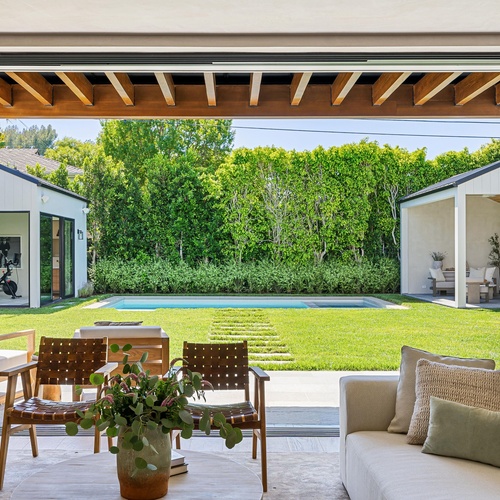 A backyard with a covered patio, open yard area, pool, another covered seating area, and small building with fitness equipment.